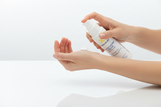 A woman holding a bottle of Glutathione Cream supplement tube and applying cream to her inner wrist